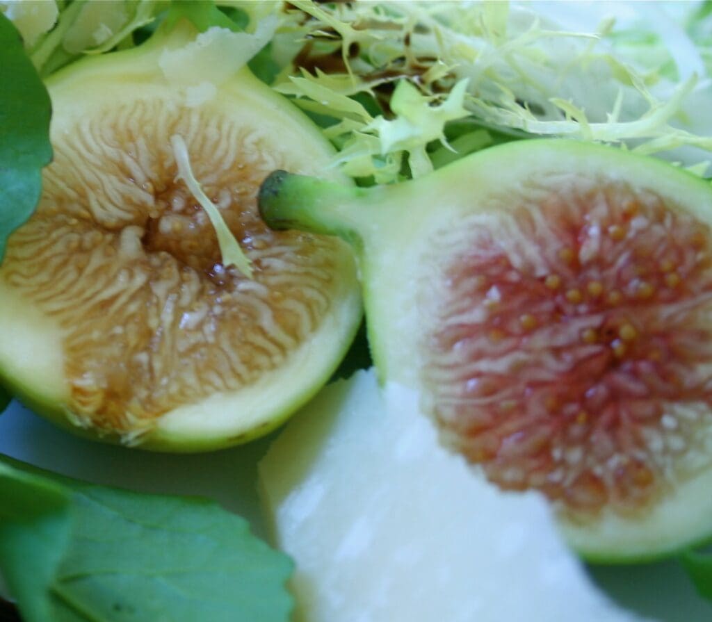 A white plate with figs and greens on it.