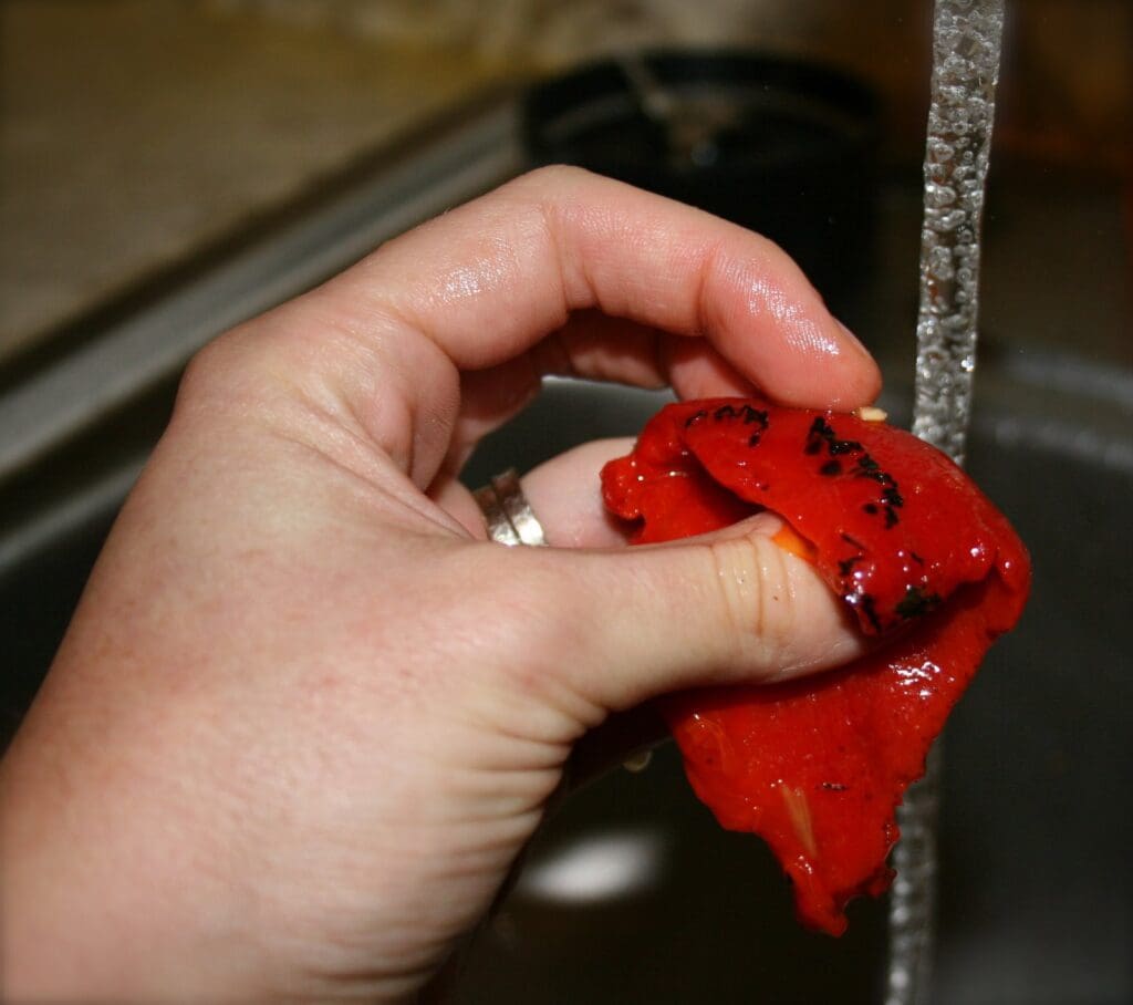 A person holding a red pepper in a sink.