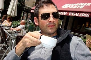A man drinking coffee at an outdoor cafe.