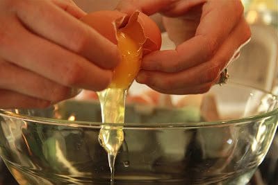 A person putting an egg into a glass bowl.