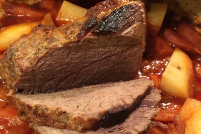 A roast is sitting in a pot of stew.