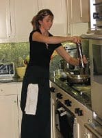 A woman in a black apron preparing food in a kitchen.