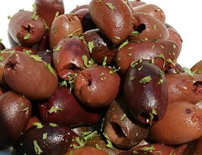 Olives on a white plate with herbs on top.