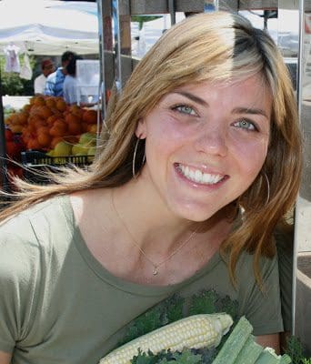A woman smiles while holding a bunch of corn.