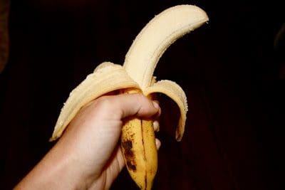 A person holding a peeled banana on a wooden table.