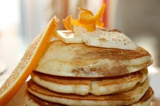 A stack of pancakes with orange slices on top.
