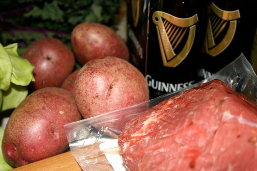Meat, potatoes and beer on a cutting board.