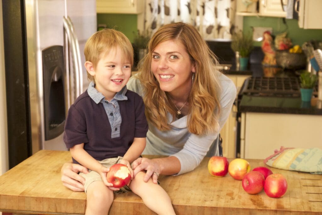 A boy and a woman seated on a kitchen counter with apples during a kids cooking camp in Los Angeles.