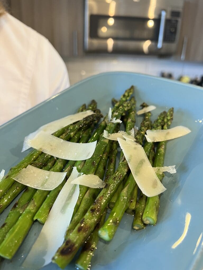 Roasted asparagus spears topped with shaved Parmesan cheese on a blue plate.