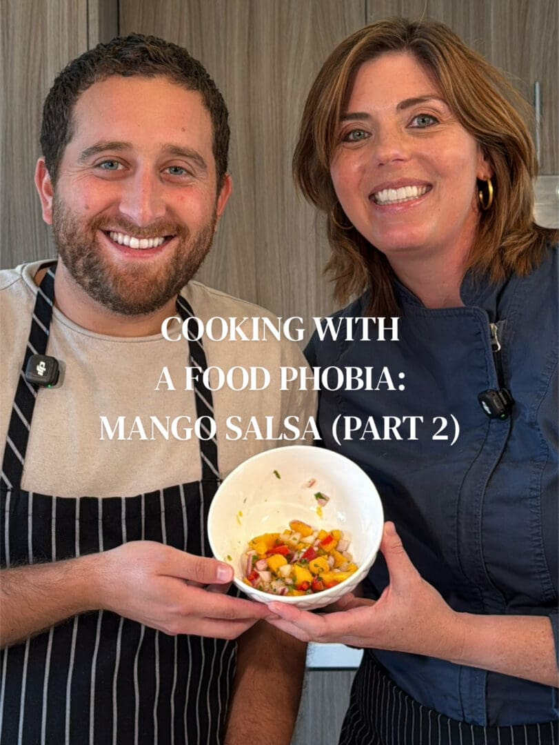 Two smiling cooks displaying mango salsa bowl