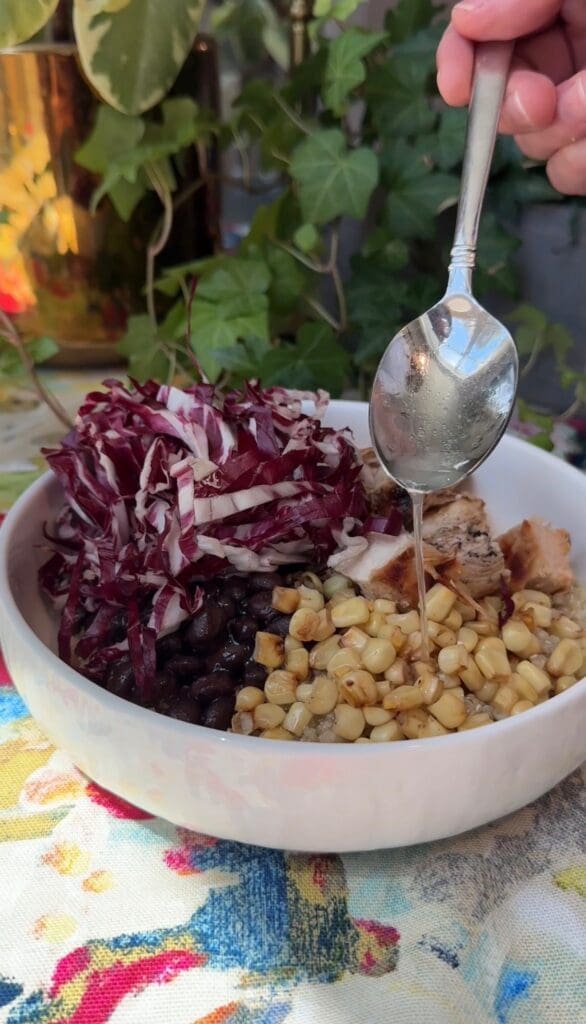 Spoon drizzling dressing over bean and corn bowl