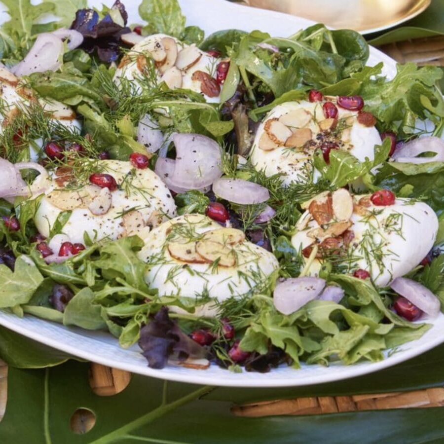 A plate with eggs, greens and pomegranate on it.