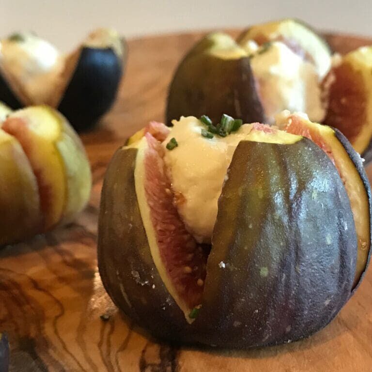 Figs stuffed with goat cheese on a wooden cutting board, drizzled with balsamic glaze.