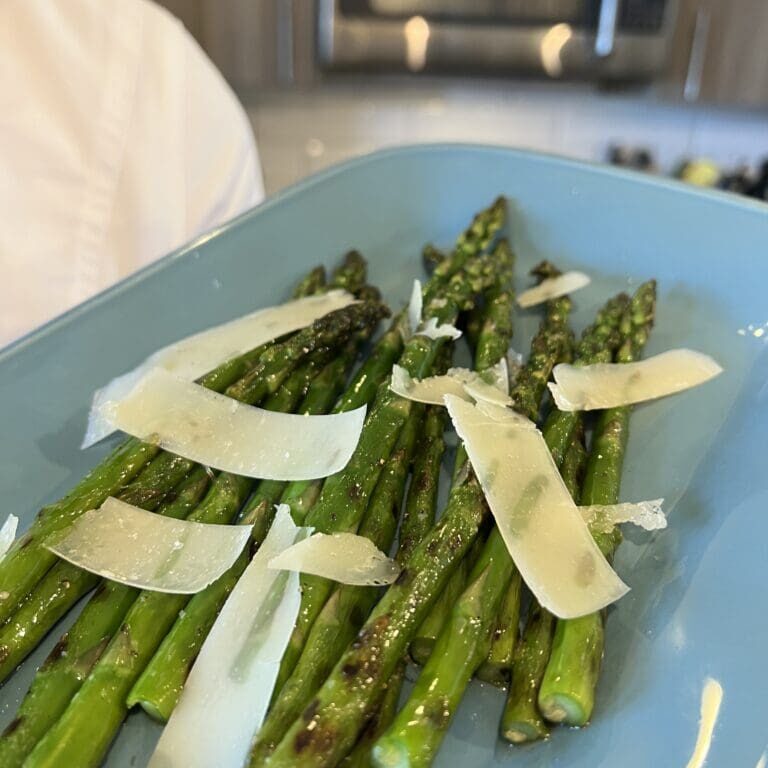 Roasted asparagus spears topped with shaved Parmesan cheese on a blue plate.