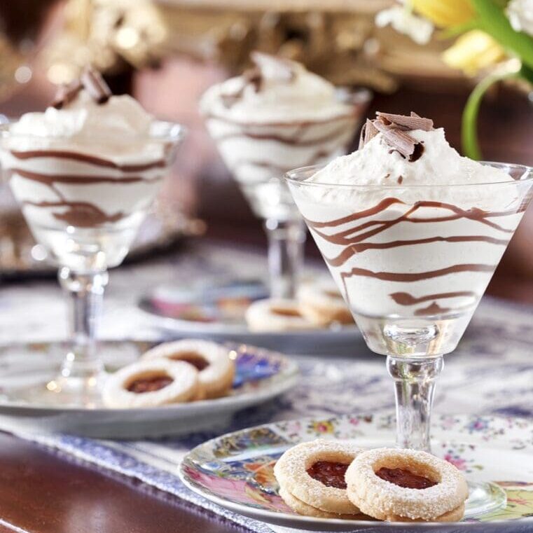 Three glasses with whipped cream and cookies on a table.