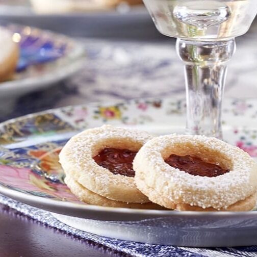 Two cookies with jam on a plate with a glass of wine.