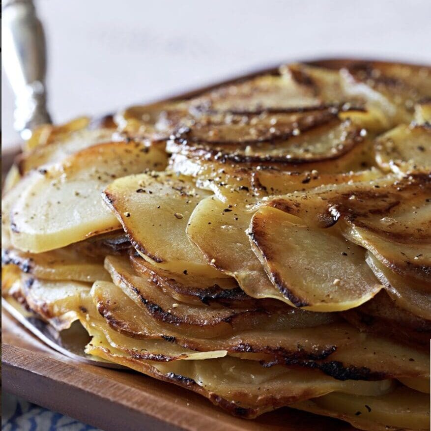 A stack of roasted potatoes on a wooden board.