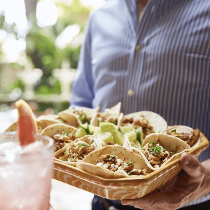 A man holding a tray of tacos and a drink.