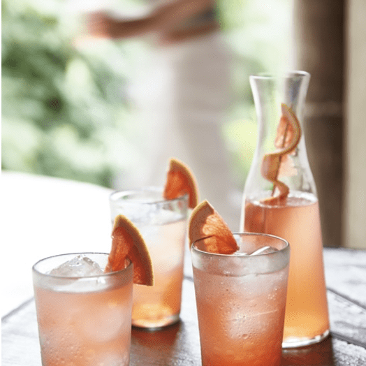 Three glasses of grapefruit infused gin and tonic on a wooden table.