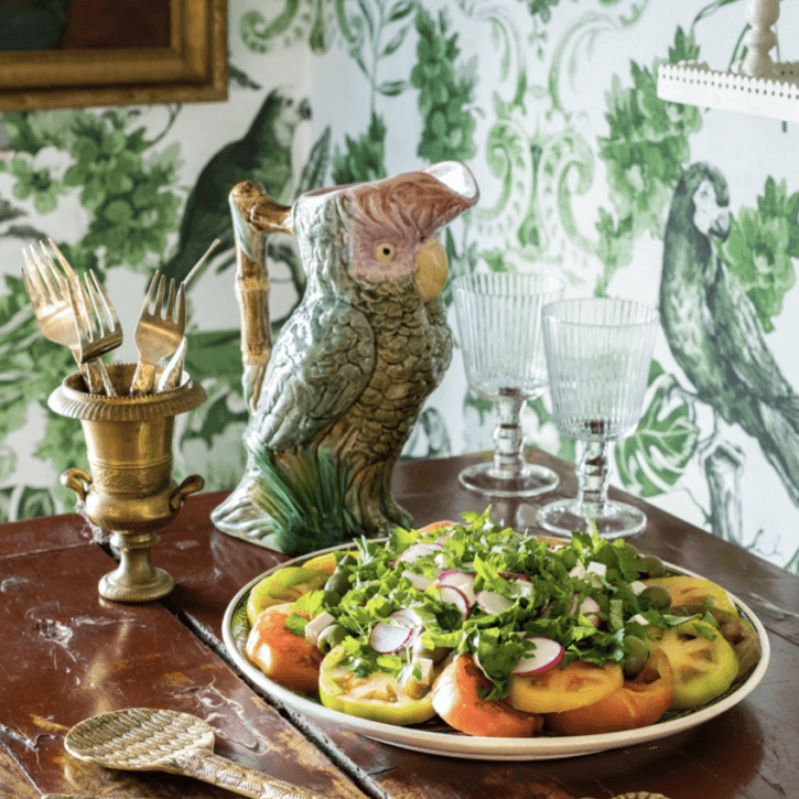 A plate of tomatoes on a table in front of a green wallpaper.