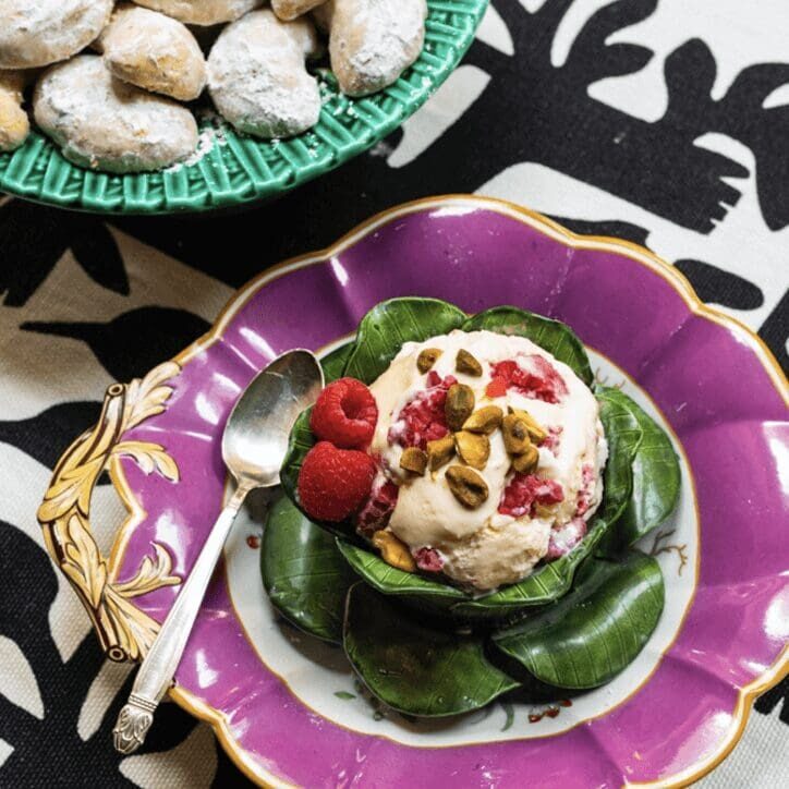 An ice cream dish with raspberries and pistachios on a purple plate.
