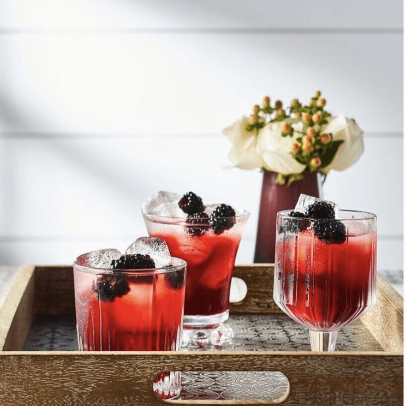Three glasses of blackberry margarita on a wooden tray.