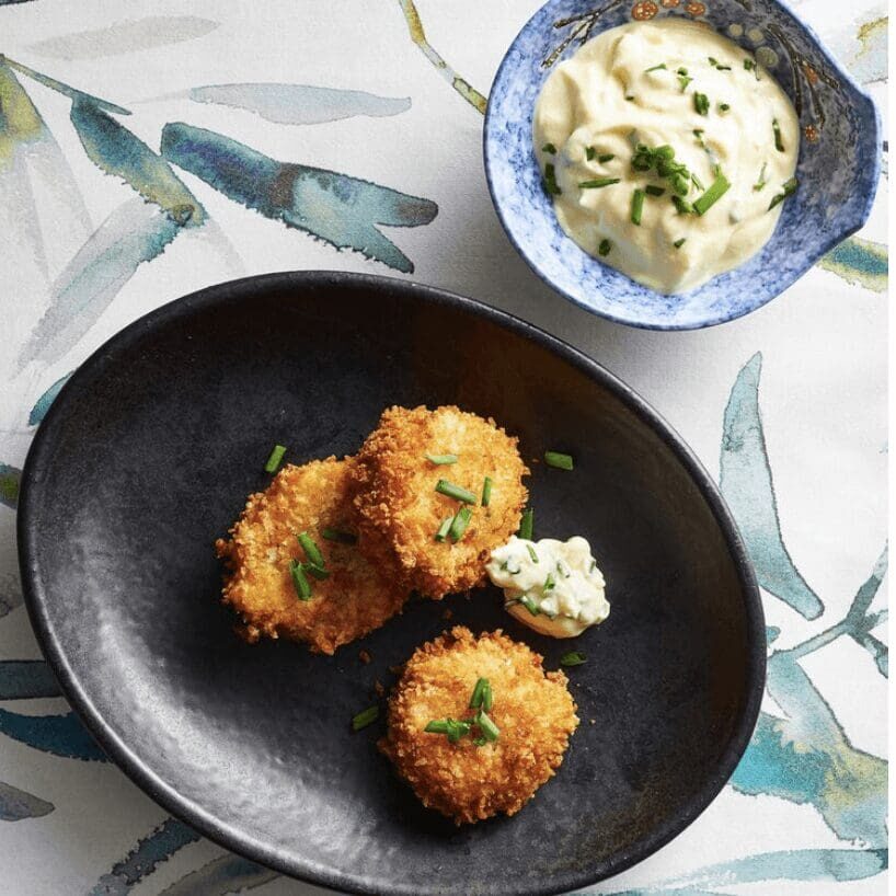 A black plate with two crab cakes and a bowl of dipping sauce.