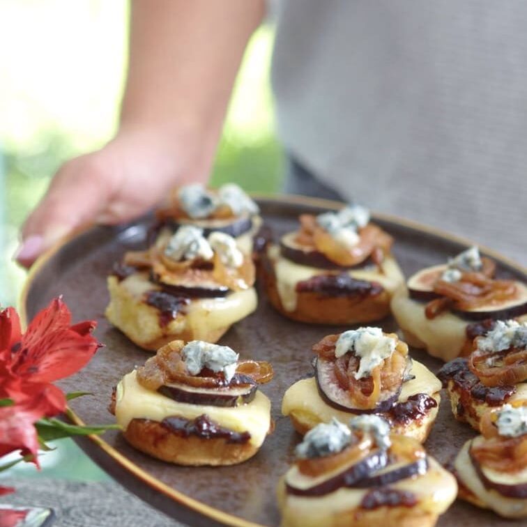 A person is holding a plate of appetizers with blue cheese and mushrooms.