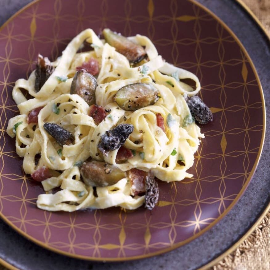 A plate of pasta with bacon and figs.